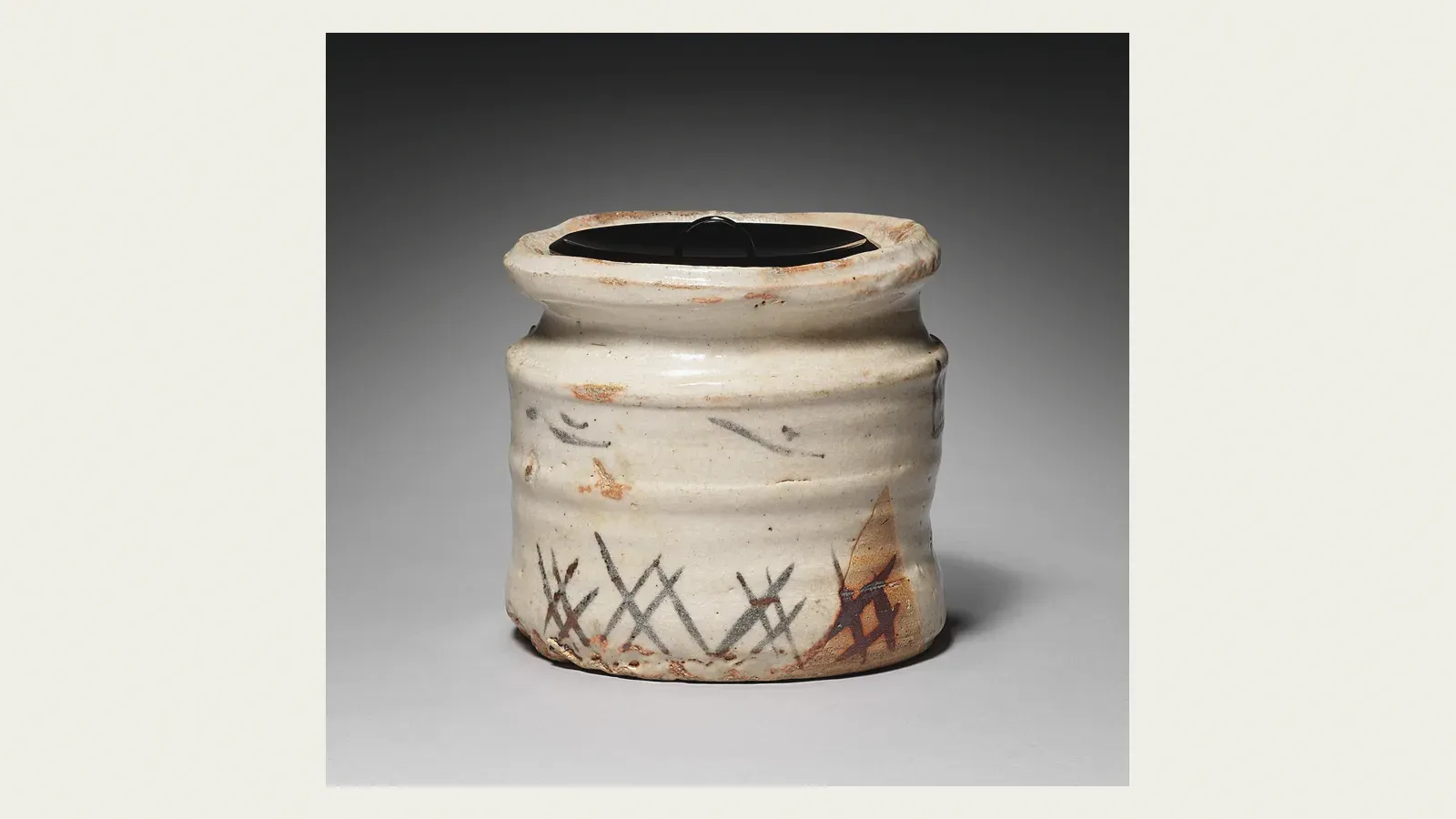 A Mino water jar, cream glaze over a ribbed body brushed with a reed fence in iron brown, capped by a black lacquer lid