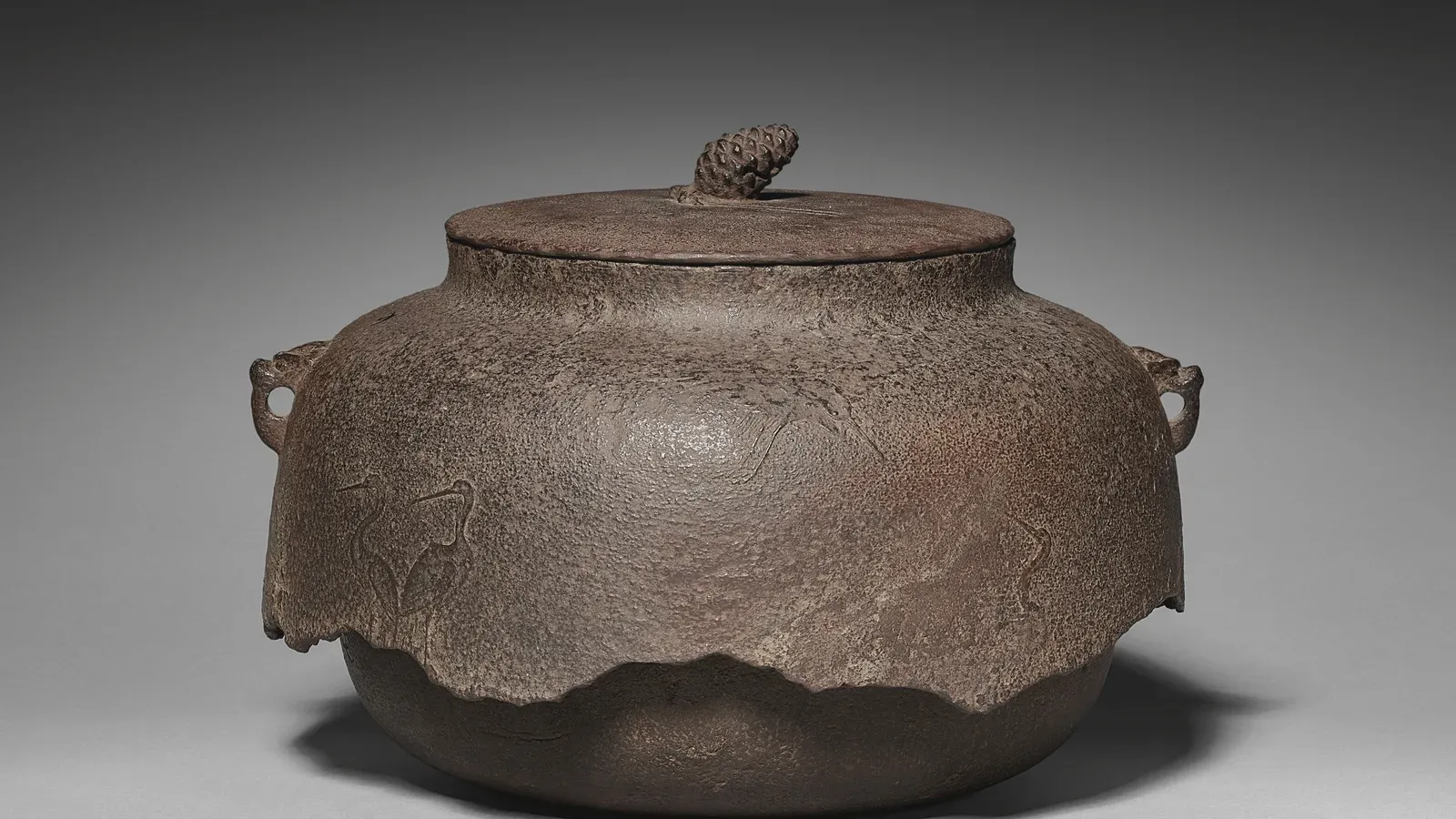 A Muromachi iron kettle with a lobed body and small side lugs, cranes cast into its skin