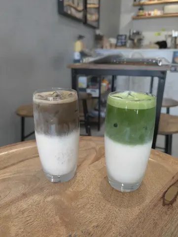 Two matcha lattes layered green over milk in tall glasses