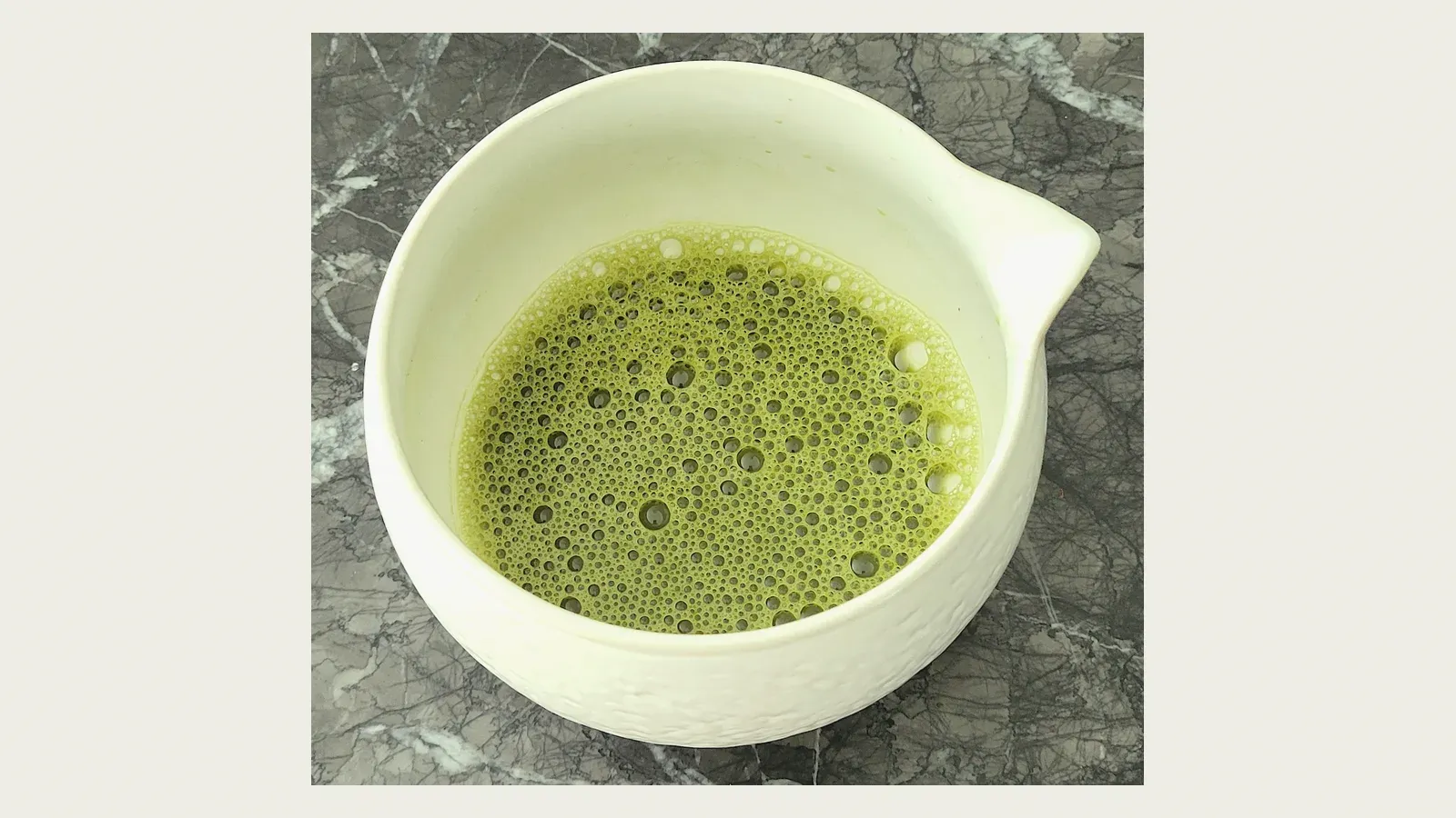 Whisked matcha standing in a pale ceramic bowl, its surface covered in fine foam