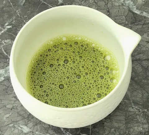 Whisked matcha standing in a pale ceramic bowl, its surface covered in fine foam