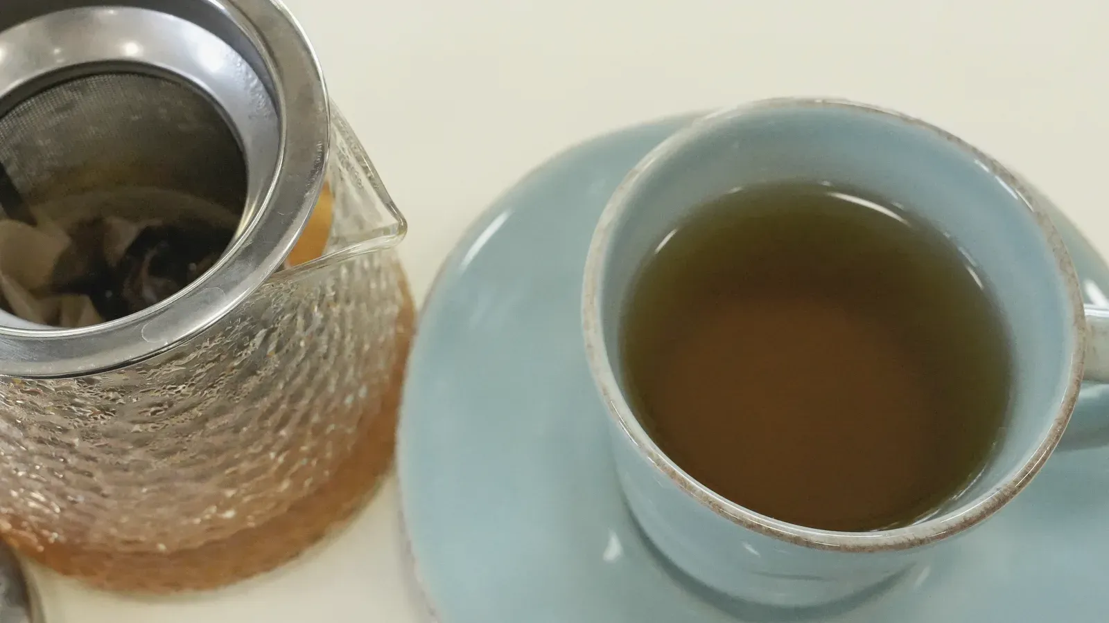 Green tea brewing in a glass pot beside a filled cup