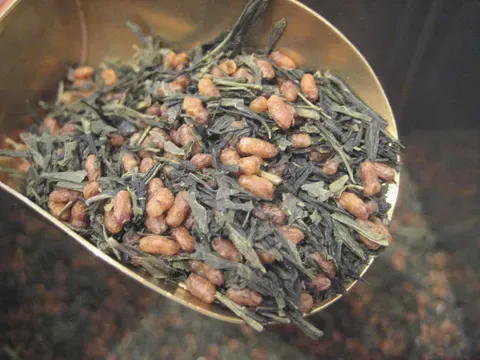 A brass scoop of genmaicha — green tea needles mixed through pale toasted rice grains