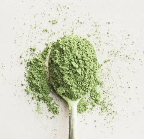 A spoonful of bright green matcha powder scattered across white paper