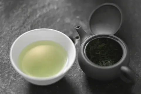 Pale jade gyokuro in a cup beside a dark side-handled pot